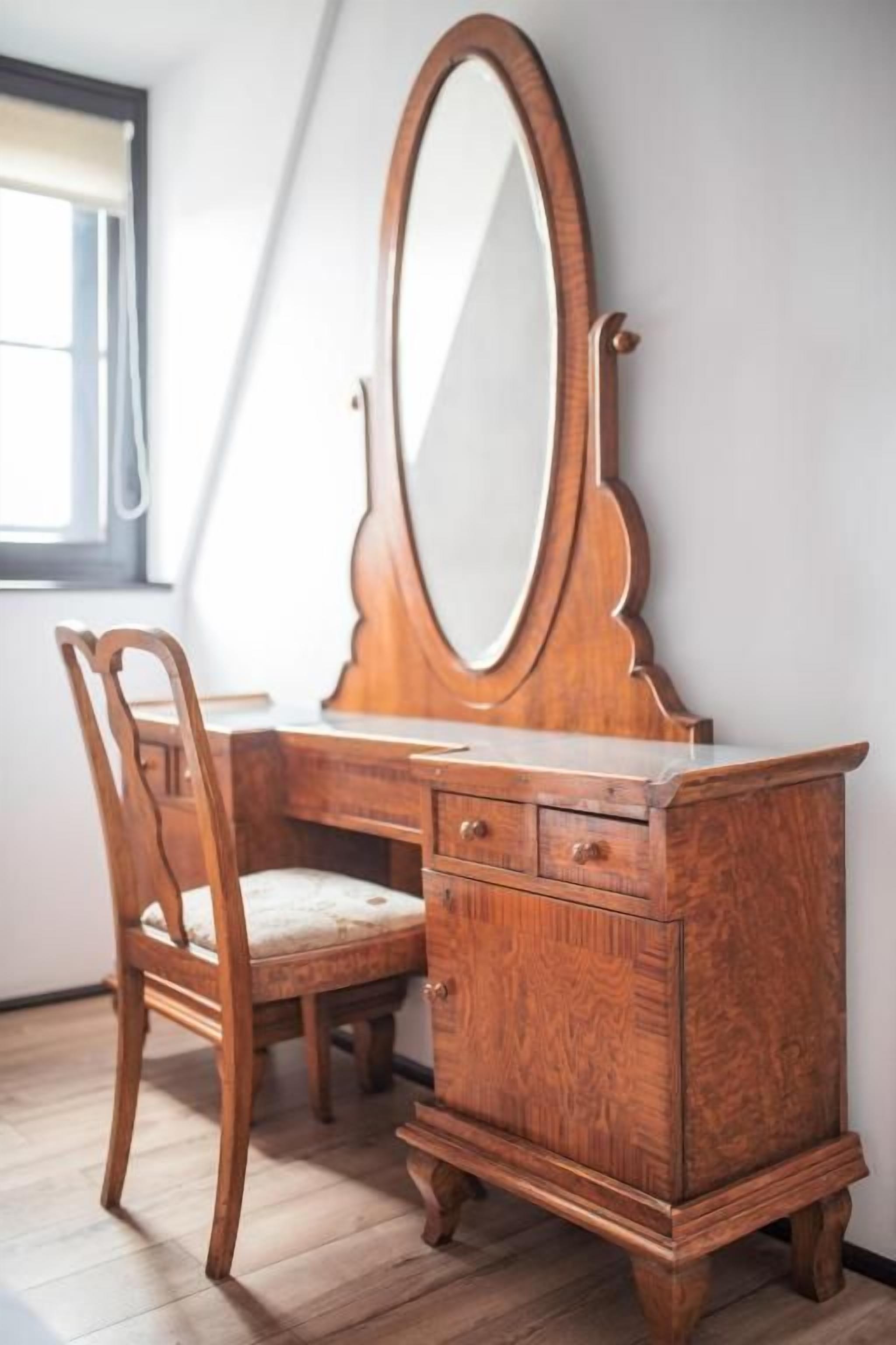 A wooden dresser with a mirror and drawers, a chair with a cushion, and a window with a curtain.