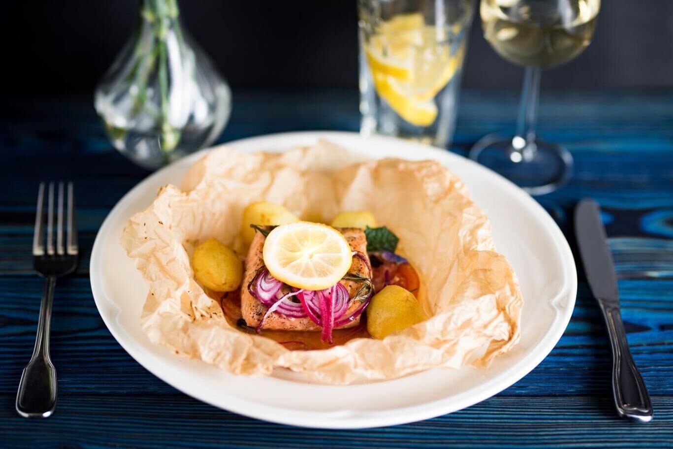 A plate of food with a lemon slice on top, surrounded by potatoes and red onions, on a white plate.