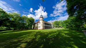 A large building with a central dome and a symmetrical facade, surrounded by a well-maintained lawn and trees. - Oficyna przy Pałacu Krobielowice (Katy Wroclawskie)