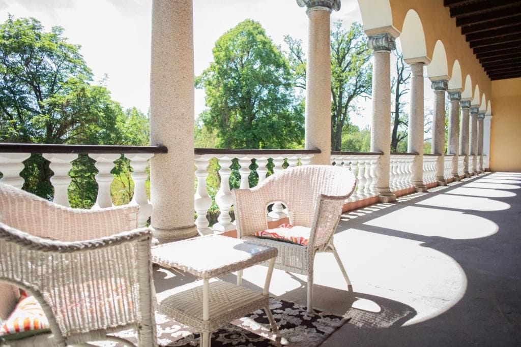 A covered outdoor seating area with wicker furniture and columns.