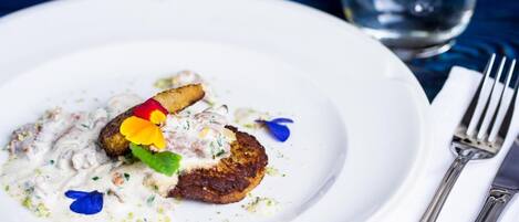 Un plato blanco con un trozo de carne, una cucharada de salsa y una guarnición de flores y hierbas.