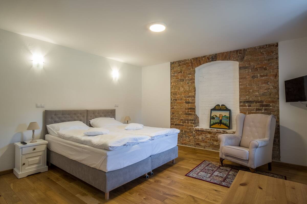 A bedroom with a bed, nightstand, chair, and a brick wall.