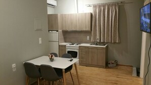 A compact kitchen with a stove, sink, and wooden cabinets. There is a dining table with chairs and a small vase of flowers. - Feanis House (Lefkada)