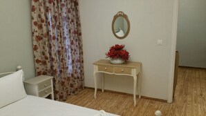 A bedroom with a bed, a bedside table with a vase of flowers, a mirror, and a wooden floor. - Feanis House (Lefkada)