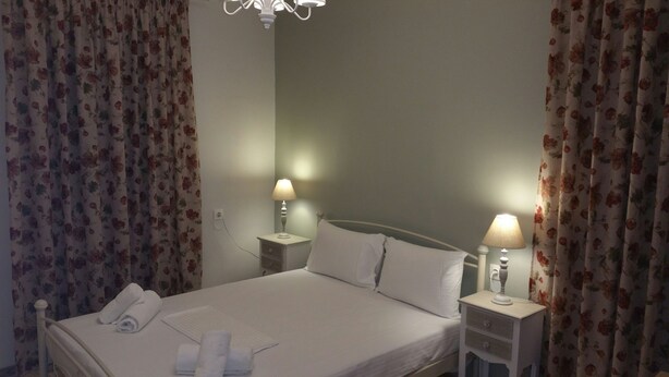 A neatly made bed with white linens, two bedside tables with lamps, and floral curtains. - Feanis House (Lefkada)