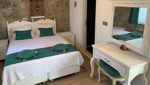 Un dormitorio con pared de piedra, cama con ropa de cama verde y blanca, cómoda blanca y espejo.