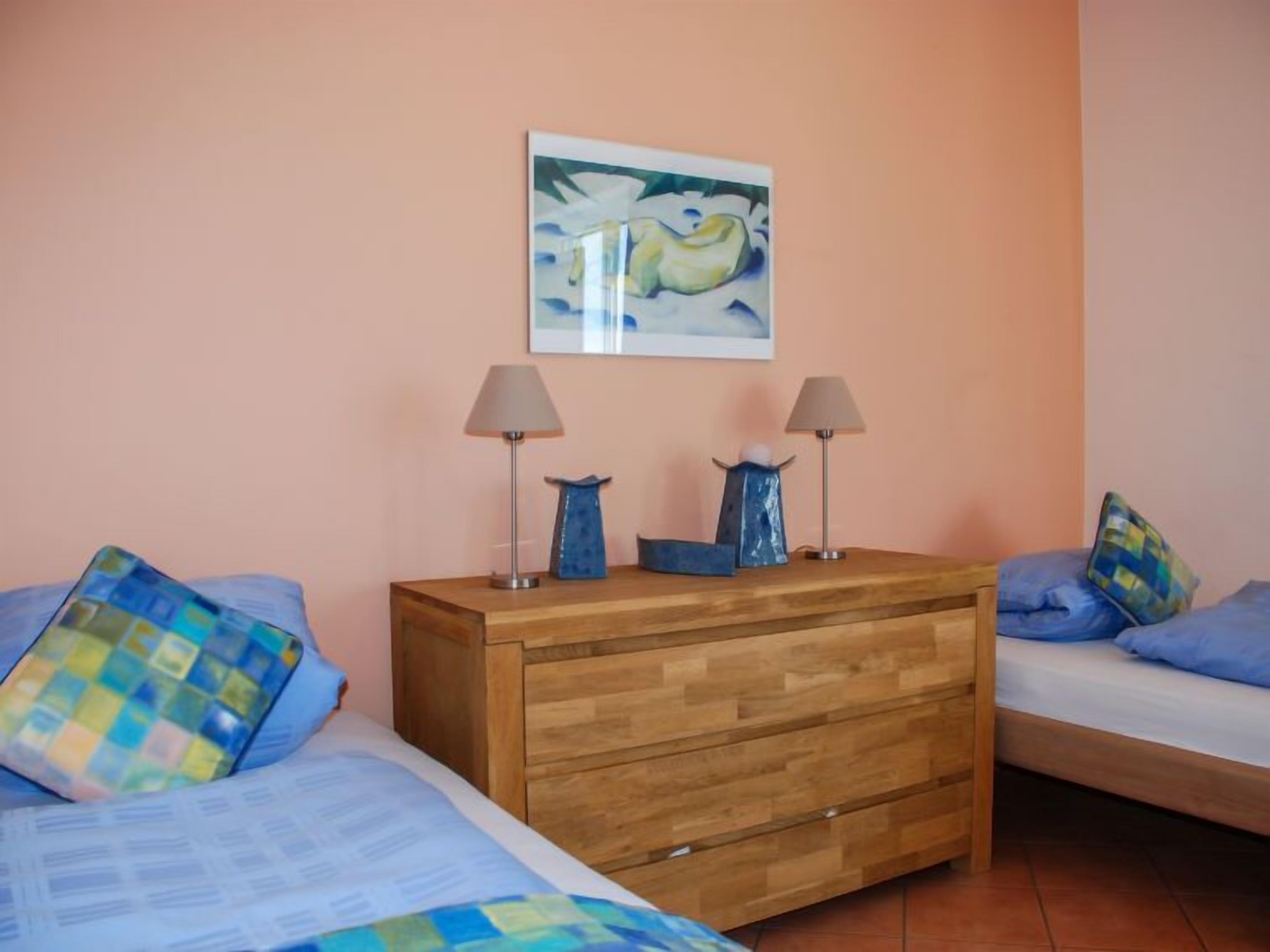 A bedroom with two beds, a wooden dresser, and a painting on the wall.