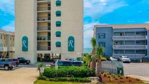 A multi-story hotel with a prominent 'R' logo on the facade, a parking lot with several cars, and a clear blue sky in the background. - Oceanfront condo w/direct beach access & 180 degree views from your private deck (Garden City Beach)