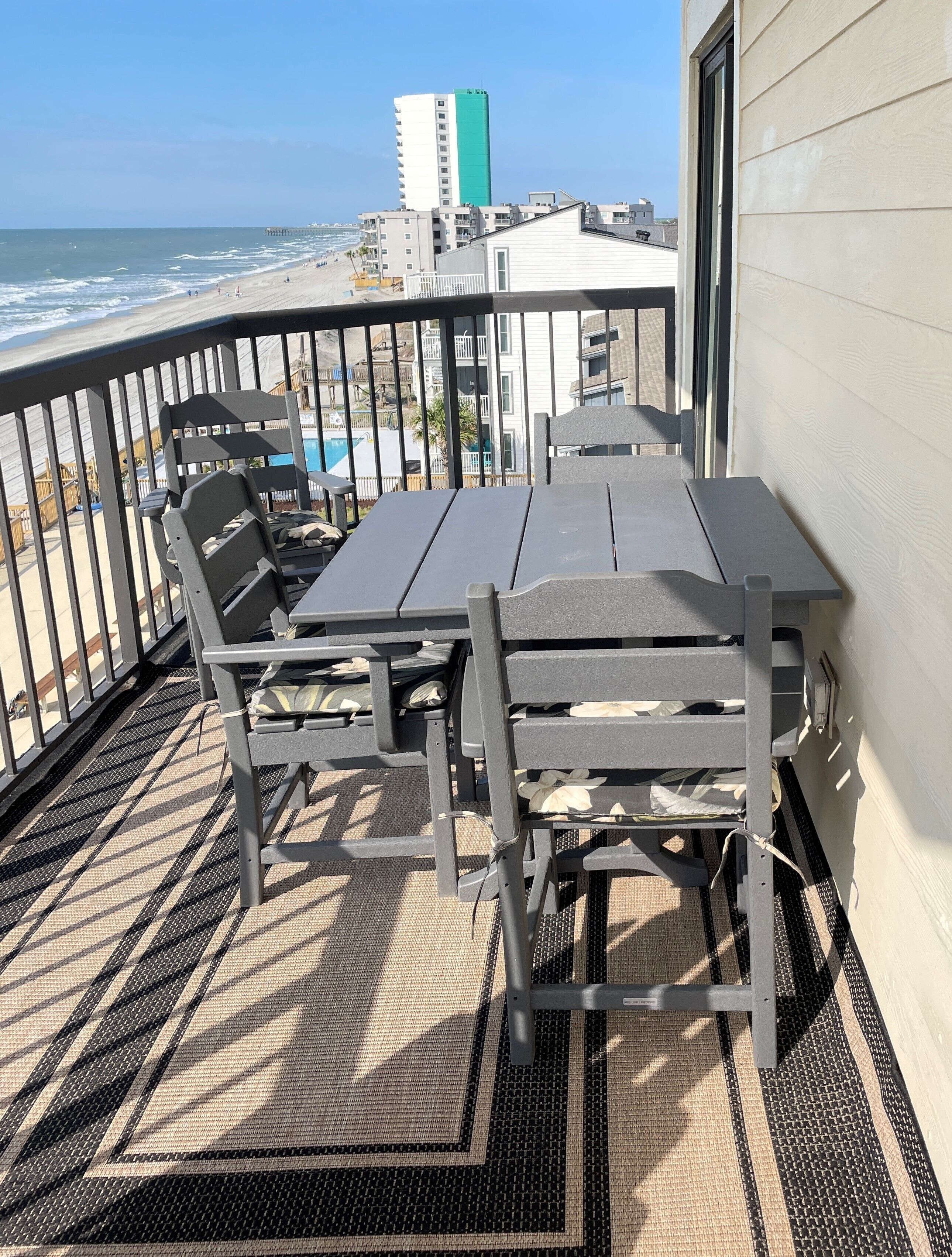 A balcony with a table and chairs, overlooking a beach and ocean.