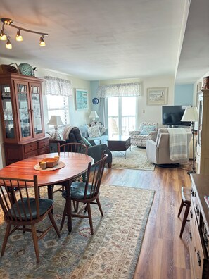 A dining area with a wooden table and chairs, a cabinet with glass doors, and a television in the background.