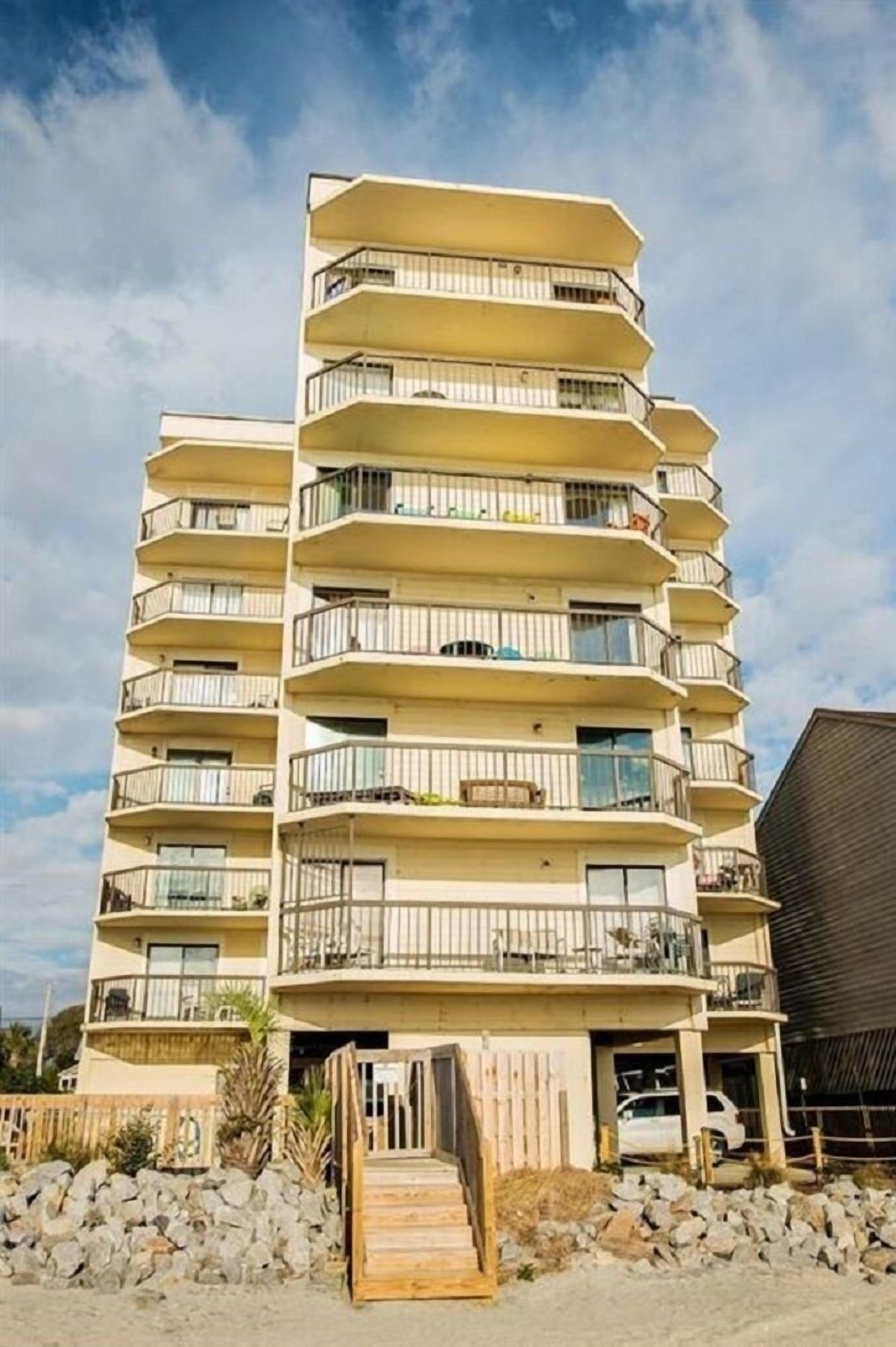 A multi-story hotel with balconies, a wooden staircase, and a parking area.