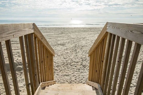 A wooden staircase leading to a sandy beach with a view of the ocean.