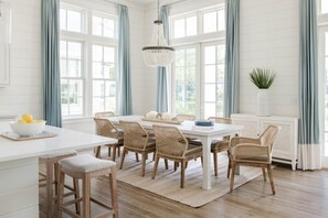 A bright kitchen with a central island, wooden chairs, and a chandelier.