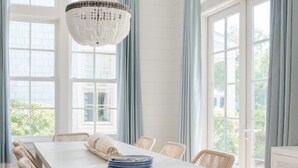 Ein Esszimmer mit weißem Tisch, Korbstühlen und einer Pendelleuchte.