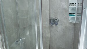 Cabina de ducha con paredes de vidrio, un lavamanos blanco y un dispensador de jabón en la pared.