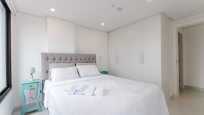 A modern bedroom with a large bed, white linens, a tufted headboard, and a teal nightstand. - Barrio Jara's Best Choice (Asunción)