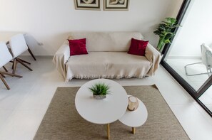 Een woonkamer met een beige bank, twee rode kussens, een klein rond tafeltje met een plant en een glazen tafel.