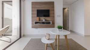 A modern living room with a mounted TV, a small shelf with decorative items, a round table with a potted plant, and a glass door leading to a balcony. - Barrio Jara's Best Choice (Asunción)