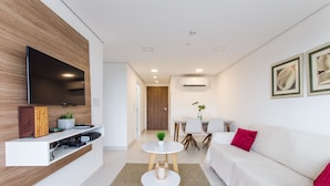 A modern living room with a flat-screen TV, a white sofa, a small round table, and a dining area with chairs. - Barrio Jara's Best Choice (Asunción)