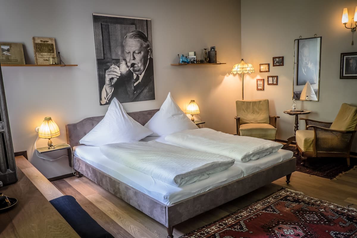 Un dormitorio ordenado con una cama grande, lámparas de noche, una silla, una mesita y una alfombra.