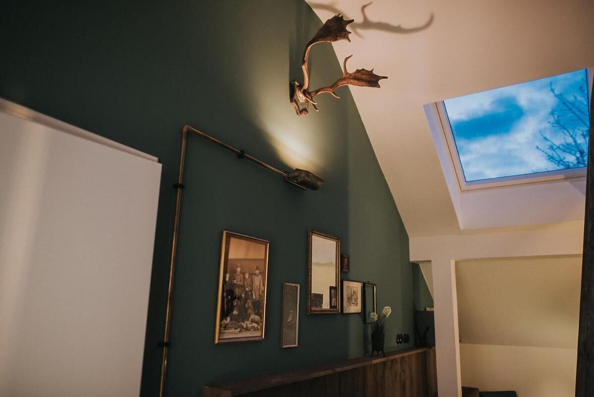 Una habitación con una pared verde oscuro, una cabeza de ciervo montada, cuadros enmarcados y un tragaluz.