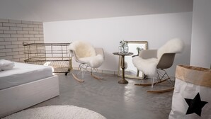 Un dormitorio moderno con una cama blanca, sillones mullidos, una mesita de noche con un espejo y un bolso estampado con estrellas.