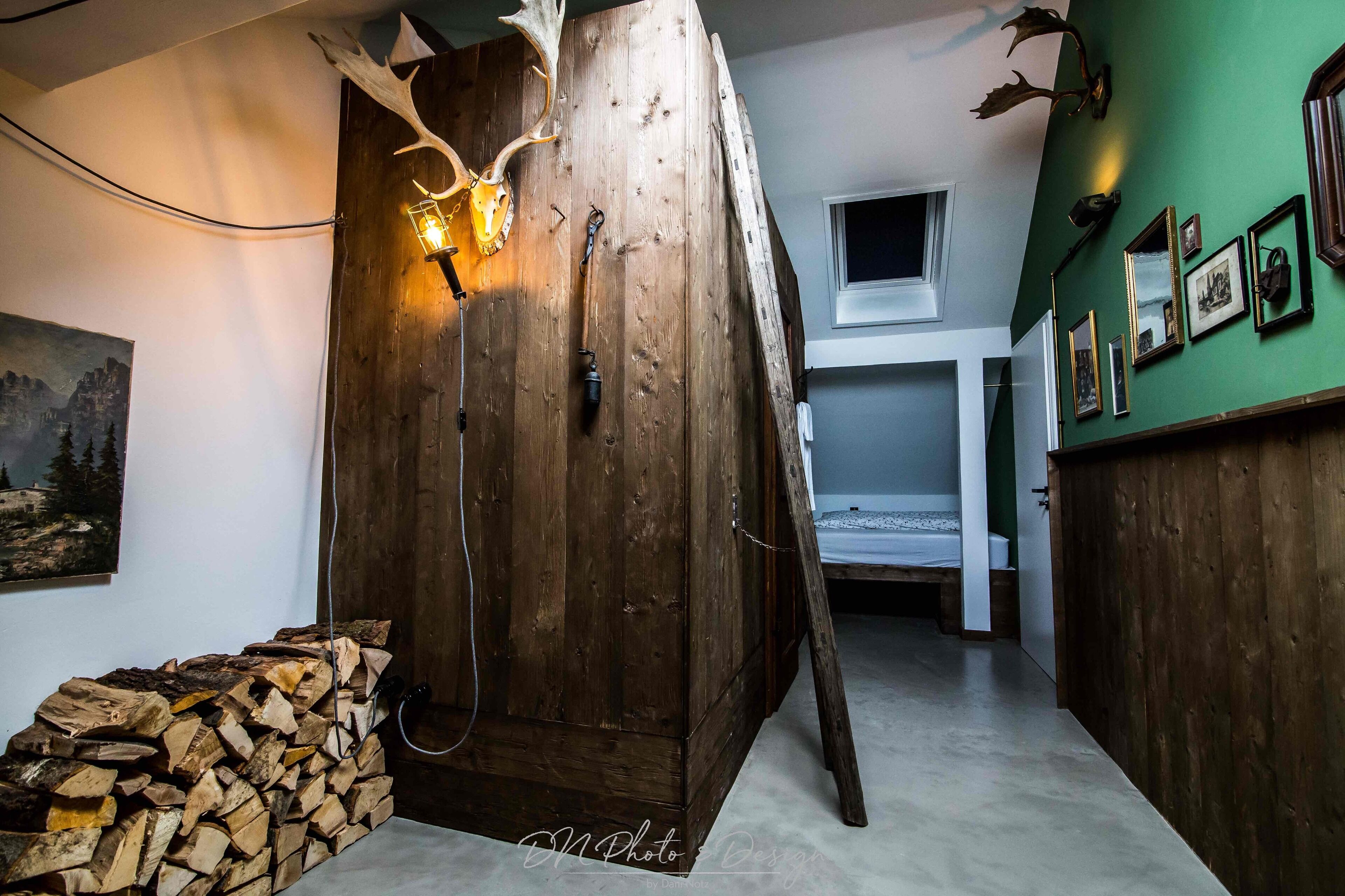 A rustic wooden room with a large wooden cabinet, a stack of firewood, and antlers mounted on the wall.