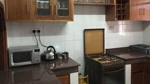A kitchen with wooden cabinets, a microwave, a kettle, and a stove. - Sheema Villas (Nairobi)