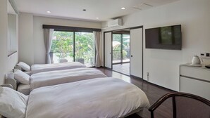 Habitación de hotel con tres camas, televisión, escritorio con hervidor y vistas a zonas verdes.