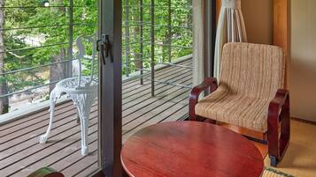 A room with a wooden deck, a chair, a table, and a view of greenery through a window with metal bars.