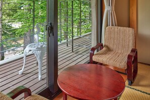 A room with a wooden deck, a chair, a table, and a view of greenery through a window with metal bars. - IKOI Villa (Karuizawa)