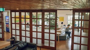 Un vestíbulo con techo de madera, un sofá de cuero negro, una mesita redonda pequeña y un panel de vidrio con paneles satinados.