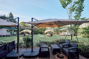 Un patio con mobiliario exterior, sombrillas y vistas a una cancha de tenis.