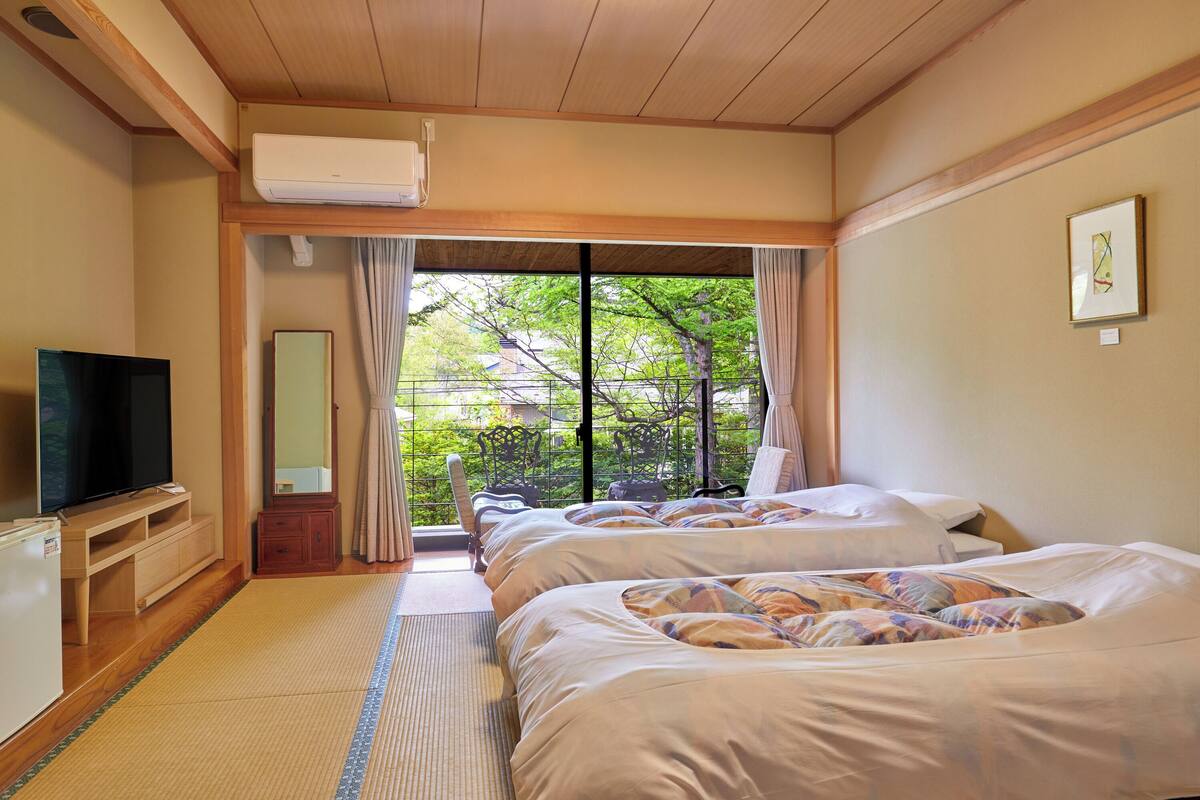 Une chambre d’hôtel avec deux lits, une télévision, un miroir et une vue sur la verdure environnante.