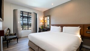A large bed with white linens, a desk with a lamp, a chair, and a window with curtains. - ANEW Hotel Hilton (Pietermartizburg)
