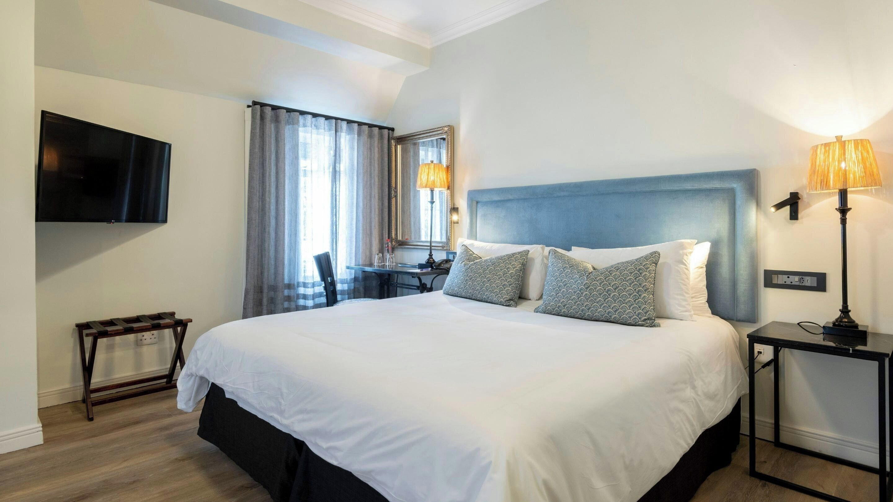 A hotel room with a large bed, a desk, a chair, a TV, and a lamp.