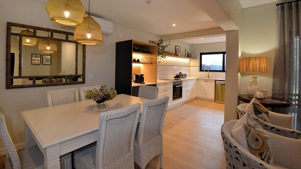 A modern kitchen with white cabinetry, a dining area with wicker chairs, and a large mirror above the counter. - ANEW Hotel Hilton (Pietermartizburg)