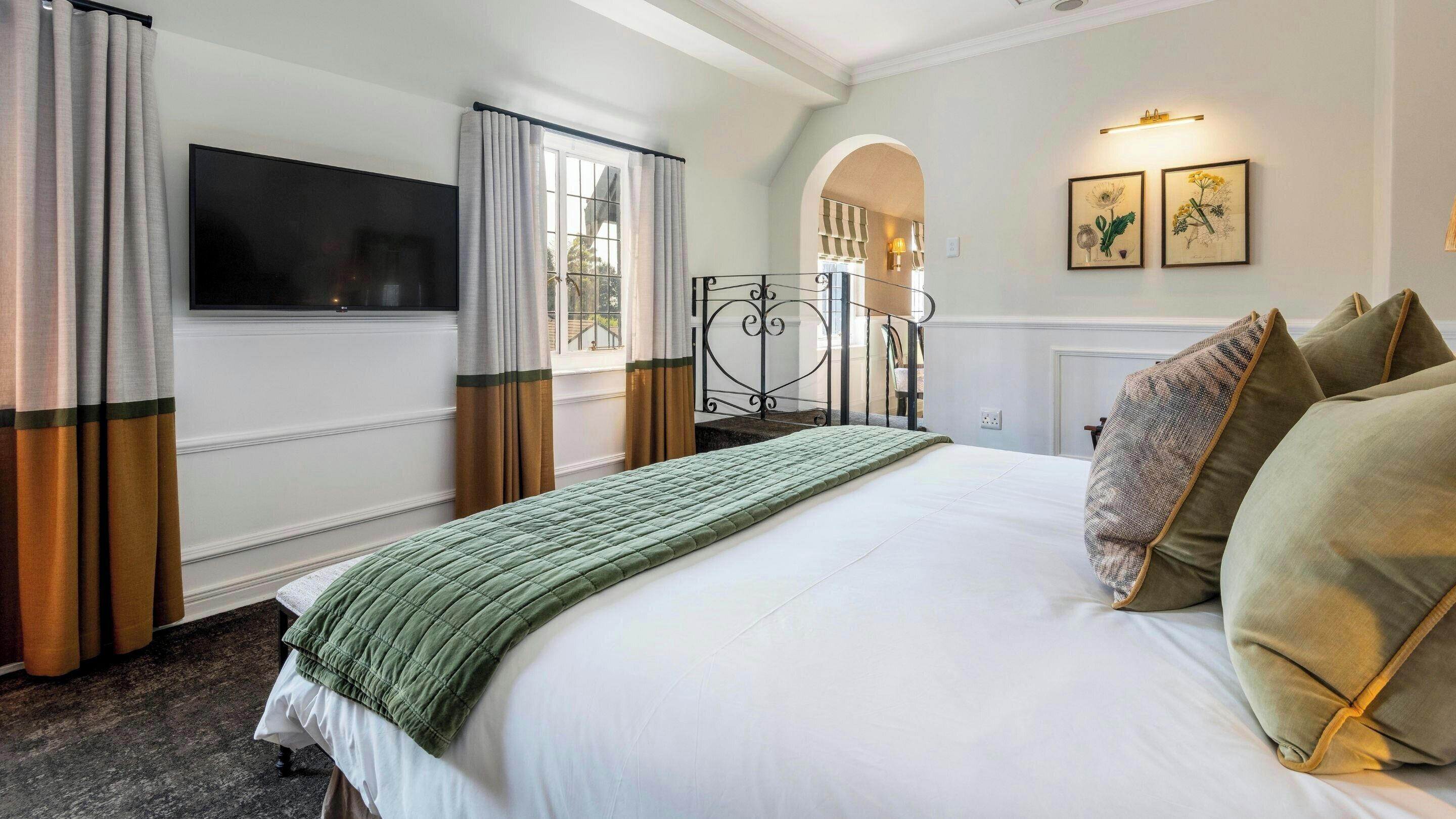 A hotel room with a bed, curtains, a television, a window, and artwork on the wall.