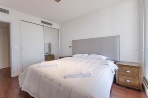 Un lit bien fait, avec une tête de lit, une table de chevet dotée d’un tiroir et une armoire avec un miroir.