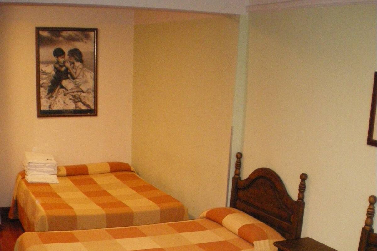 A room with two beds, each with a checkered bedspread, a wooden nightstand, and a framed picture on the wall.