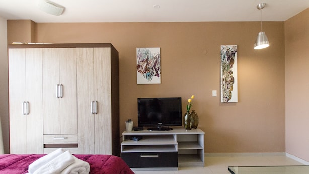 Ett hotellrum med en säng, en tv, en garderob och konstverk på väggarna.
