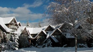 Un grupo de cabañas de madera con techos nevados y árboles, ubicadas en un paisaje cubierto de nieve.