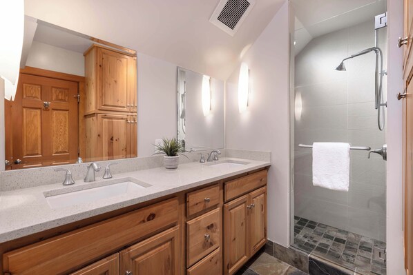 A bathroom with a wooden vanity, a large mirror, a shower with a handheld showerhead, and a towel hanging on a rack.