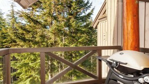 A balcony with a grill, wooden railing, and a view of dense forest.
