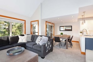 A modern living room with a sofa, a dining table, and a kitchen area.