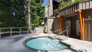 A swimming pool with a wooden deck and metal railings, surrounded by a fence and trees.