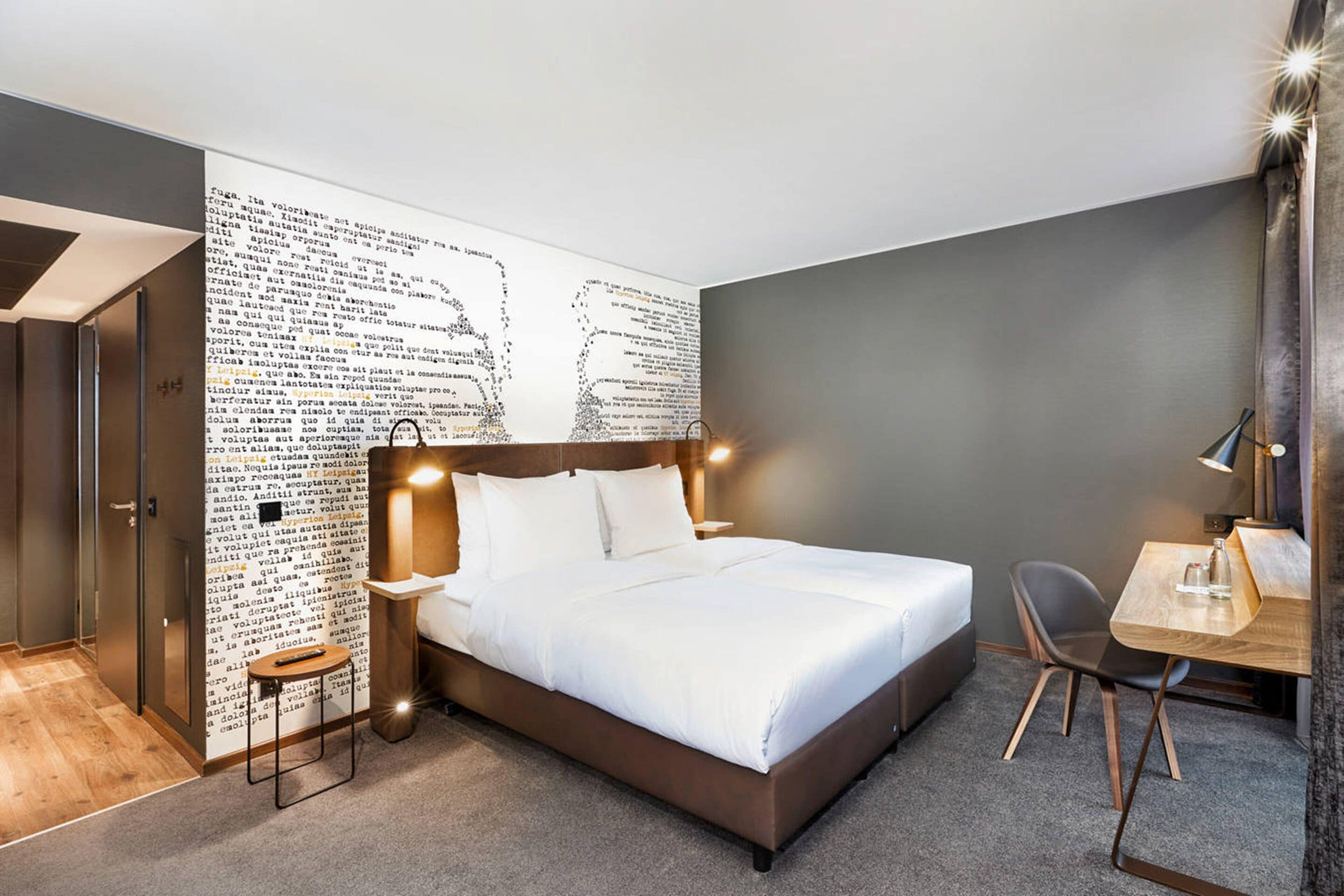 Una habitación de hotel moderna con una cama grande, un escritorio y una pared con un diseño de texto original.
