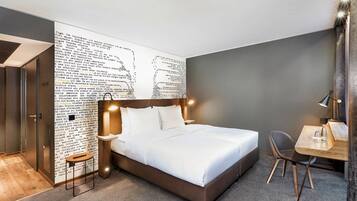 Una habitación de hotel moderna con una cama grande, un escritorio y una pared con un diseño de texto original.
