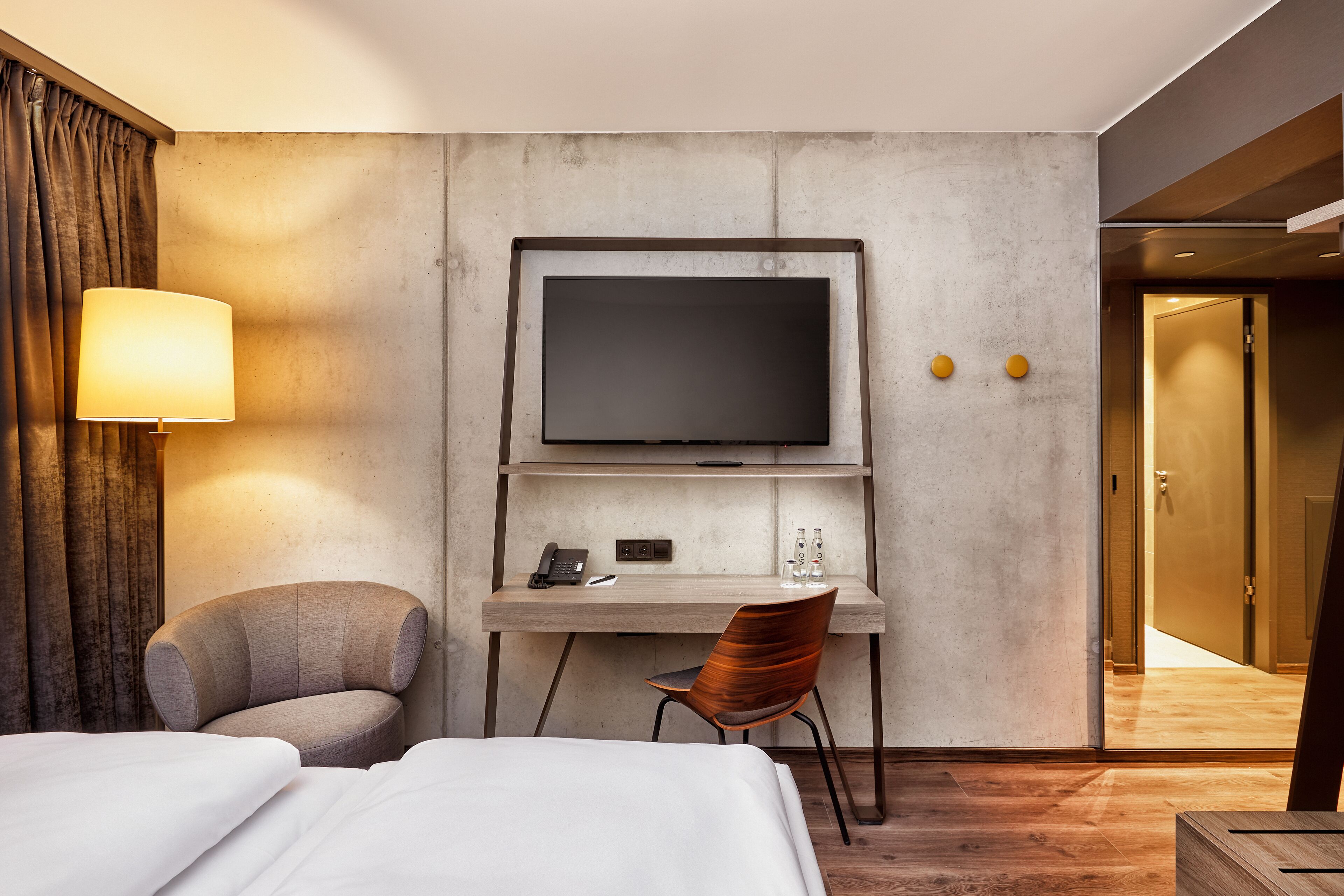 Una habitación de hotel con una cama, un escritorio con televisor de pantalla plana, una silla y una lámpara.