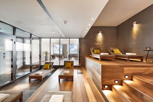 Un moderno espacio de spa con suelo de madera, un mostrador de recepción y zonas de estar con cojines.